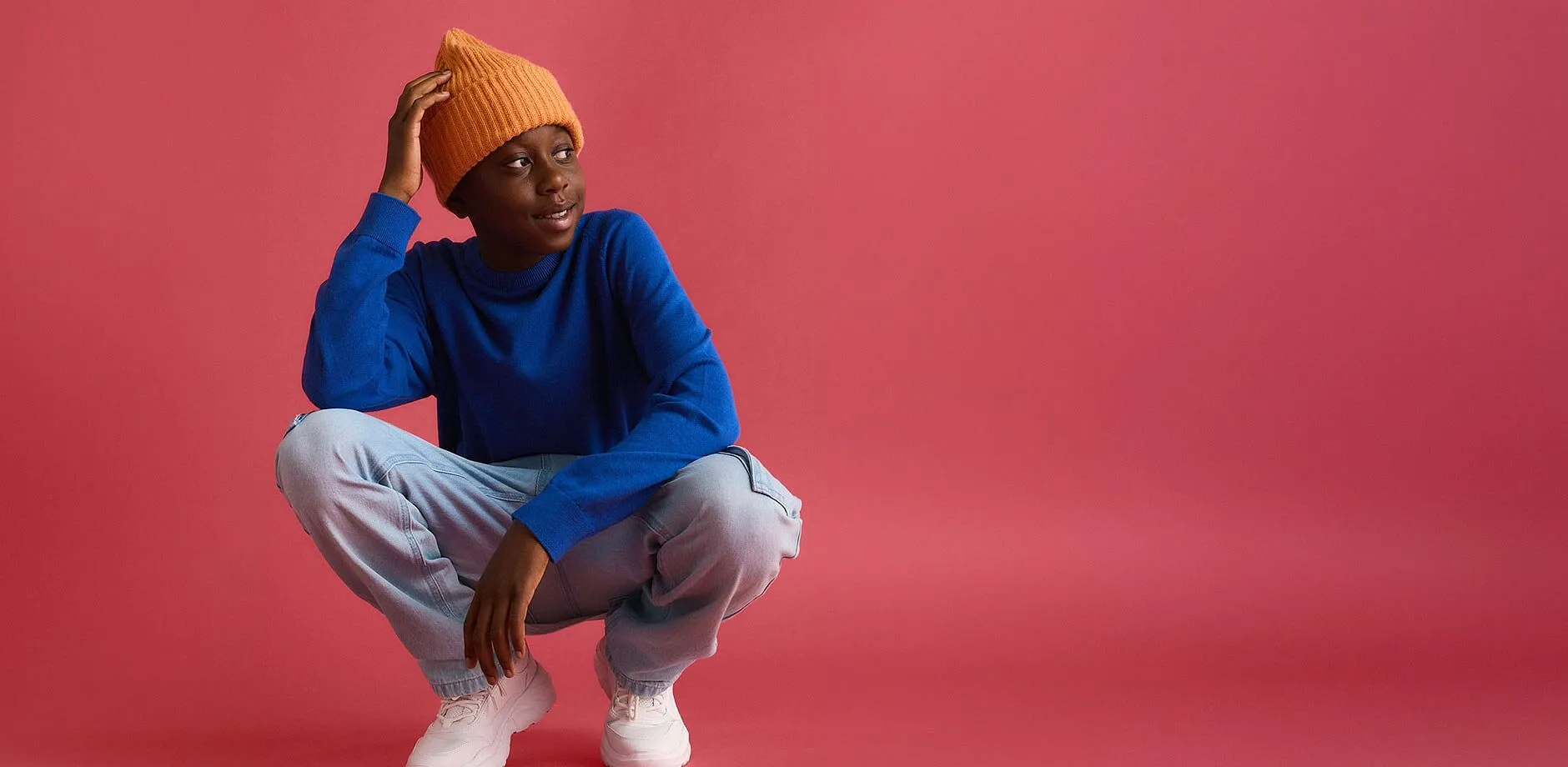 Orange M&uuml;tze, blauer Pullover, helle Jeans und wei&szlig;e Turnschuhe.
