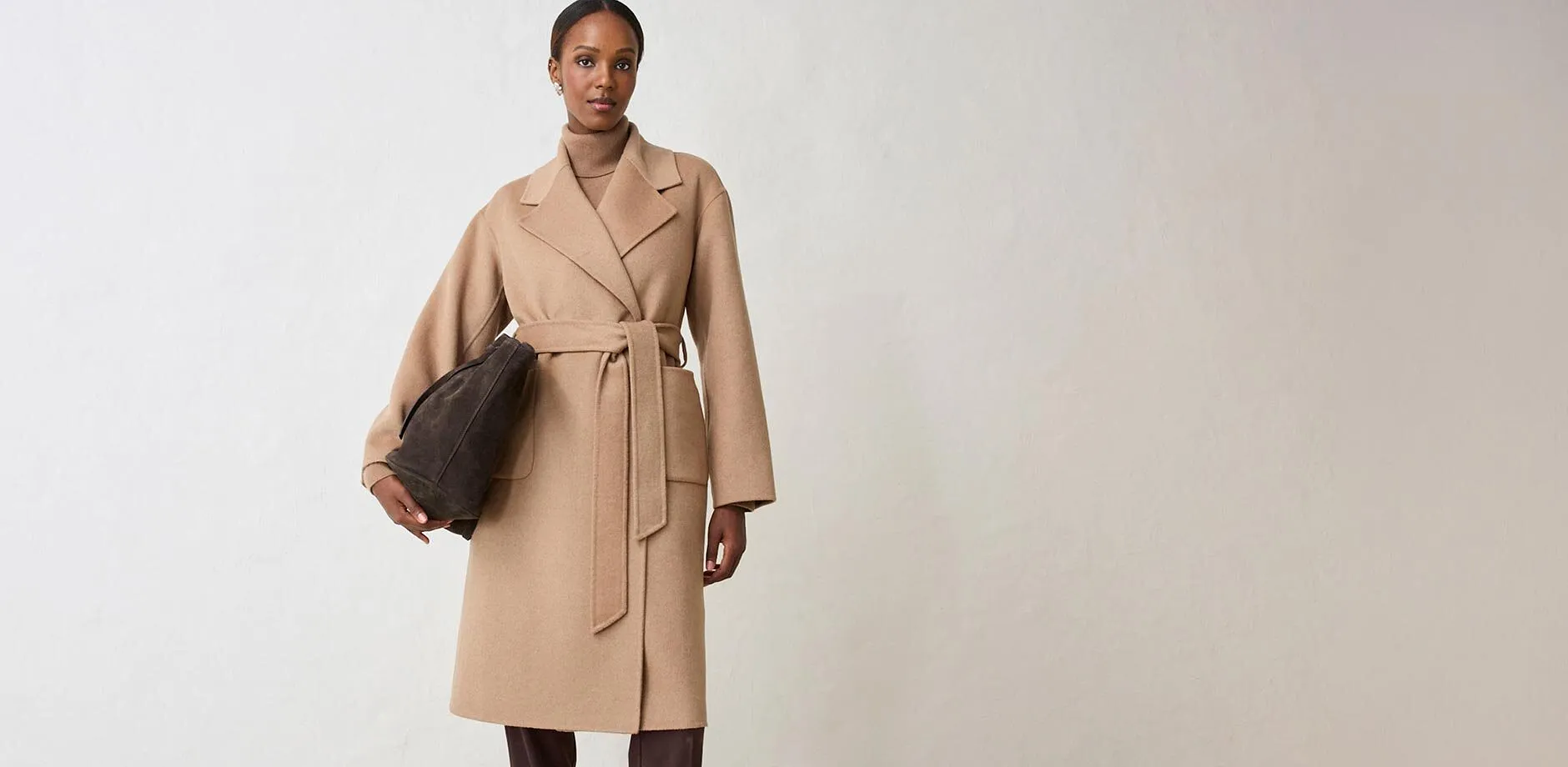 Manteau crois&eacute; beige &eacute;l&eacute;gant, pull &agrave; col roul&eacute; en dessous, compl&eacute;t&eacute; d'un sac de couleur fonc&eacute;e.