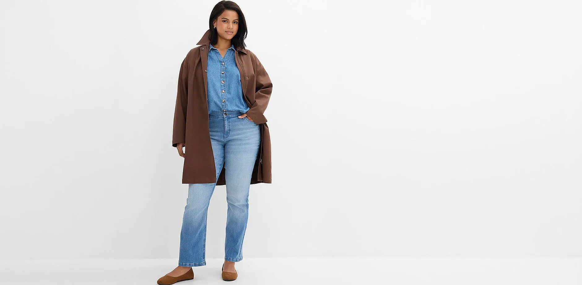 Manteau marron par dessus une chemise en jean, jean clair et chaussures marron confortables.