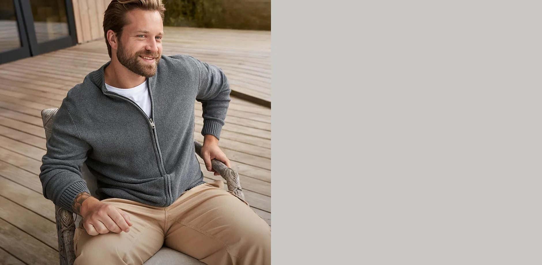 Er tr&auml;gt eine graue Strickjacke &uuml;ber einem wei&szlig;en T-Shirt und beige Hose.