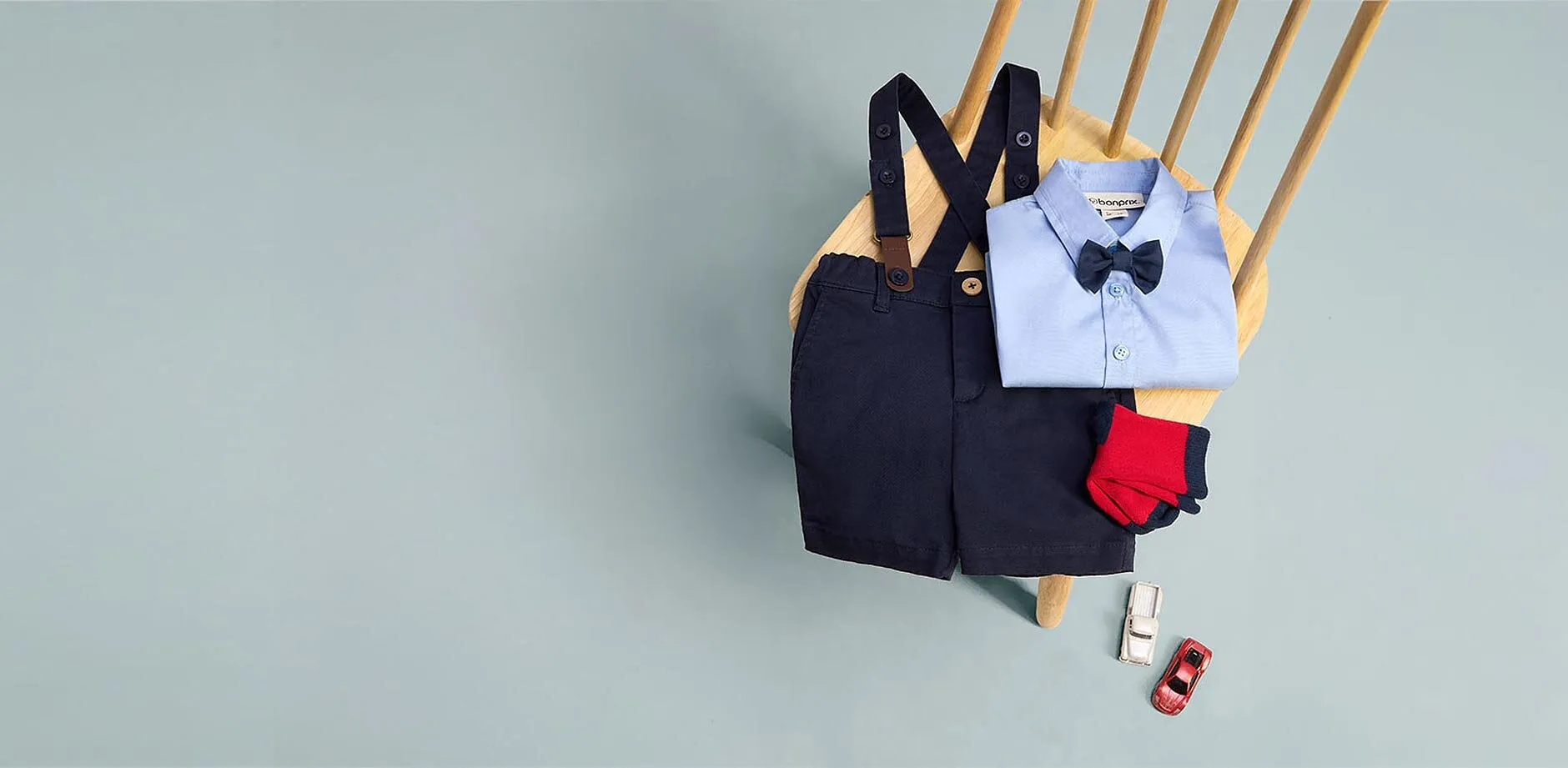 Blaue Latzhose, hellblaues Hemd, Fliege, rote Socken und Schuhe.