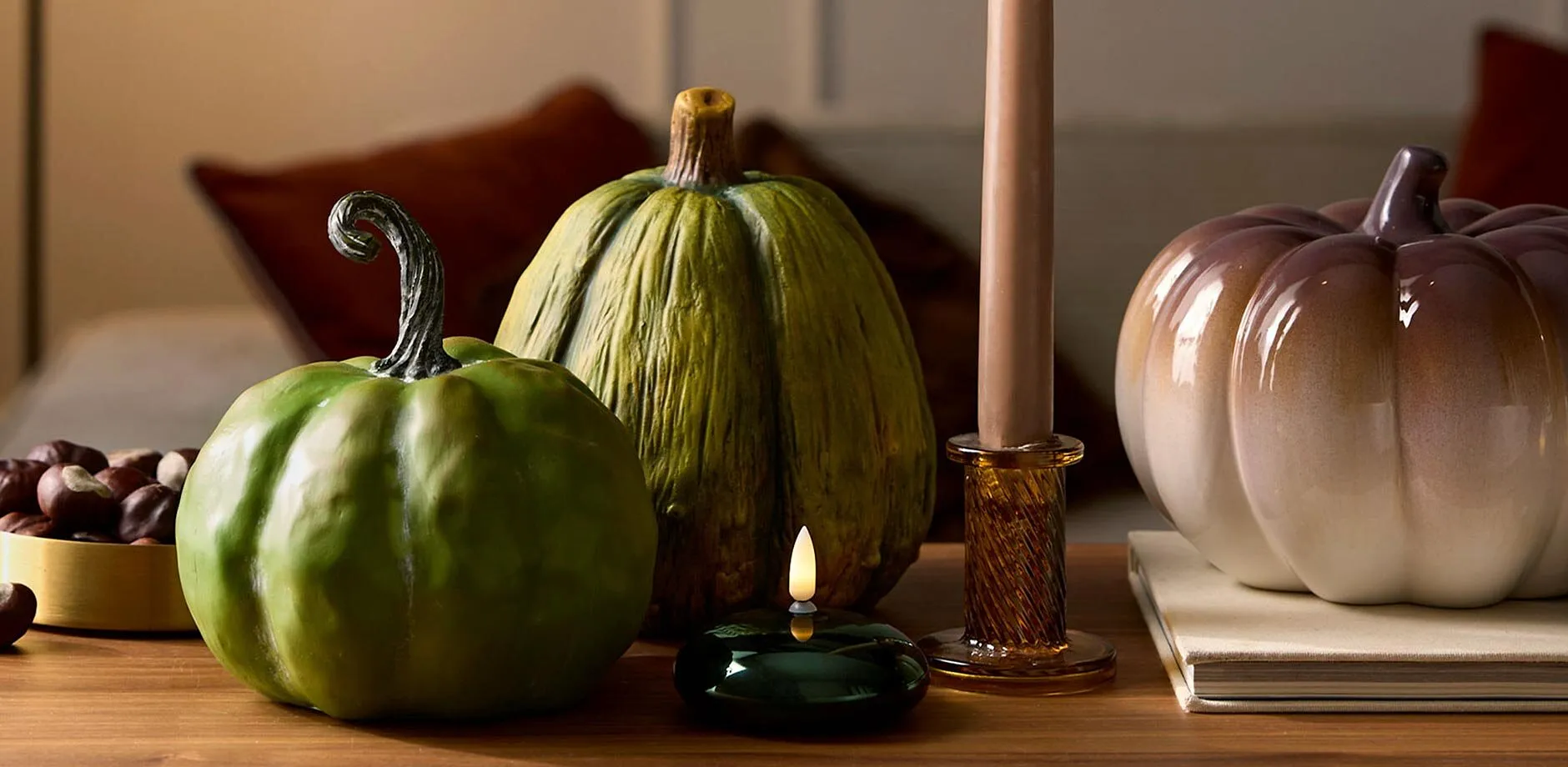 Une d&eacute;co d'automne chaleureuse et cosy avec des bougies, des citrouilles d&eacute;coratives et des ch&acirc;taignes sur un support bois. 