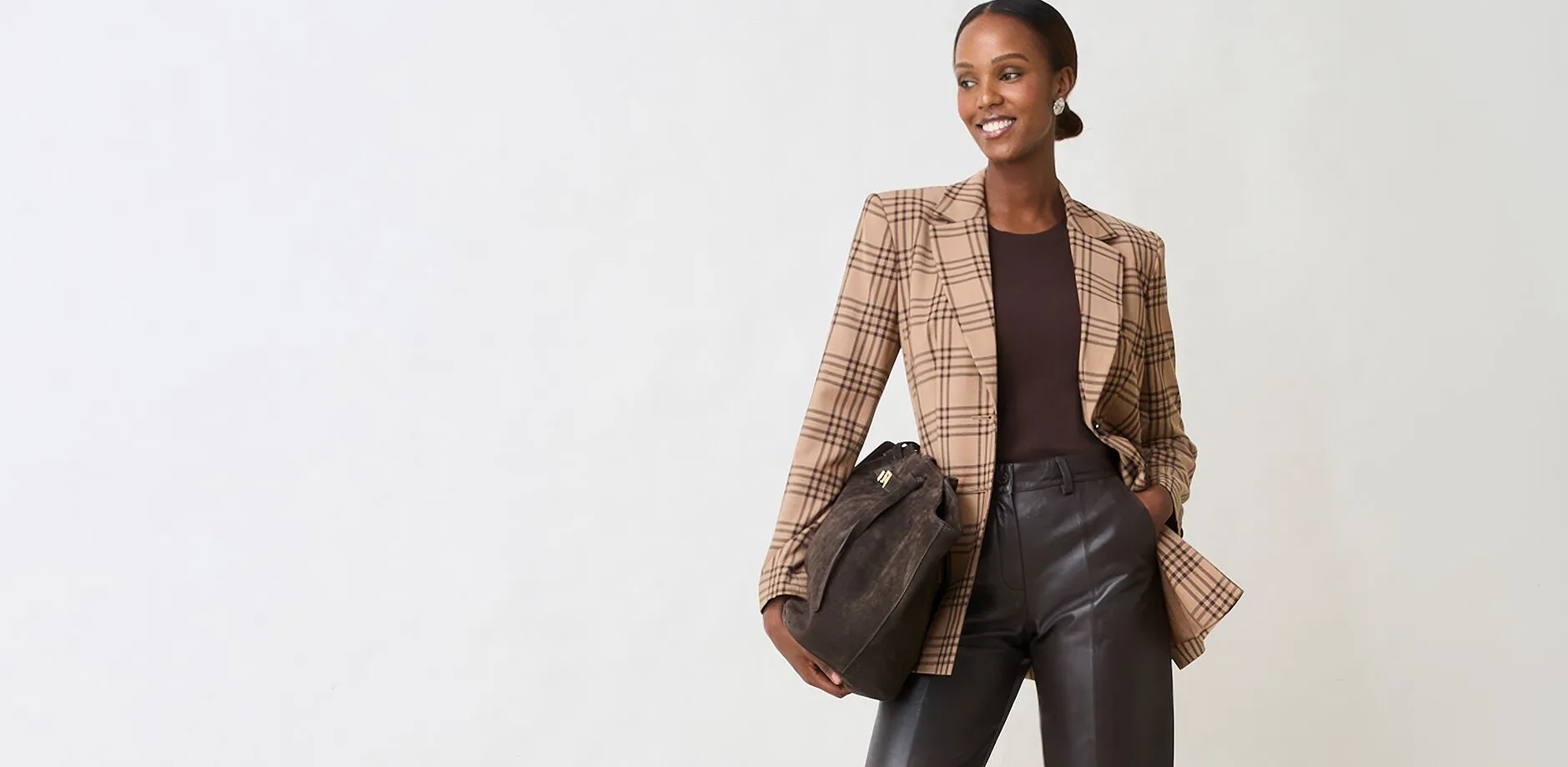 Karierter Blazer, dunkles Top, Lederhose und Wildleder-Tasche ergeben einen schicken Look.