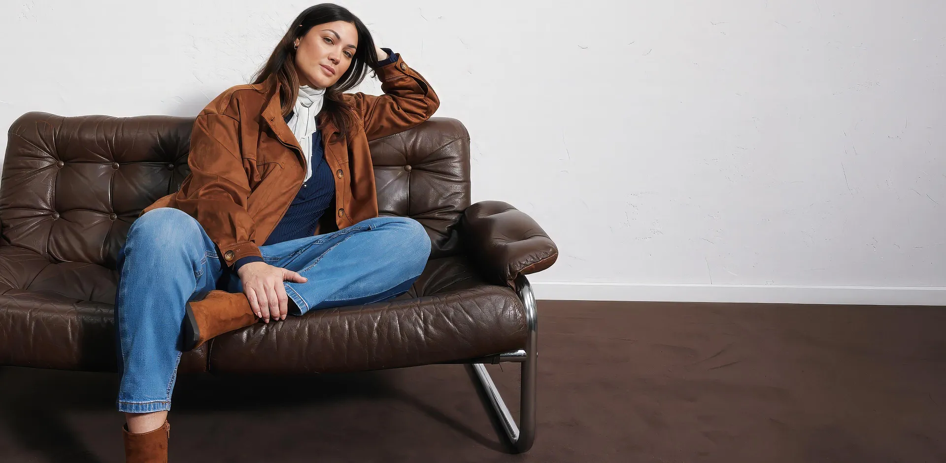 Veste en synth&eacute;tique marron, jean bleu, haut fonc&eacute;, &eacute;charpe claire et bottes.