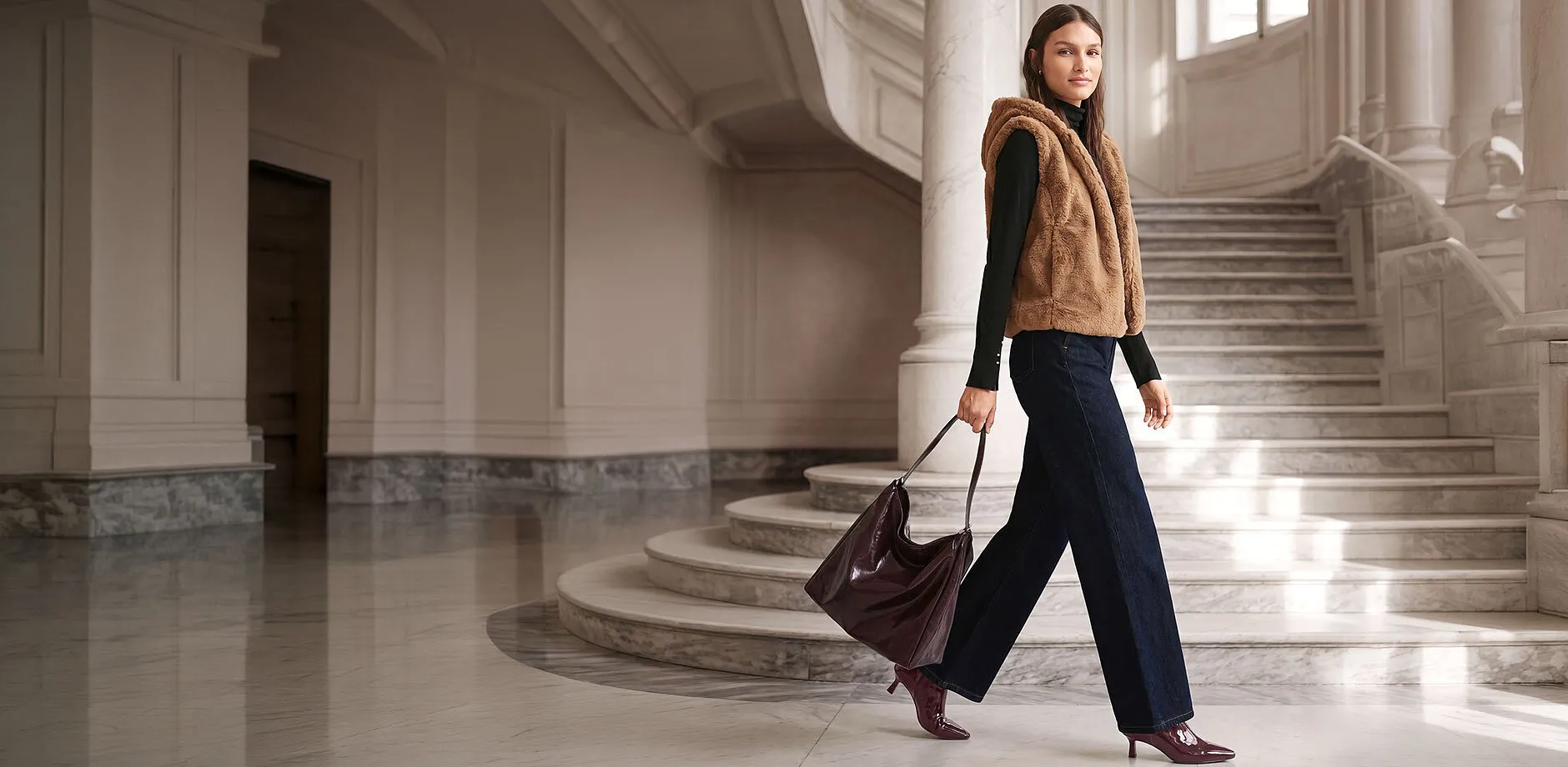 Braune Fellweste, schwarzer Rolli, weite Jeans, burgunderfarbene Tasche und Stiefeletten.
