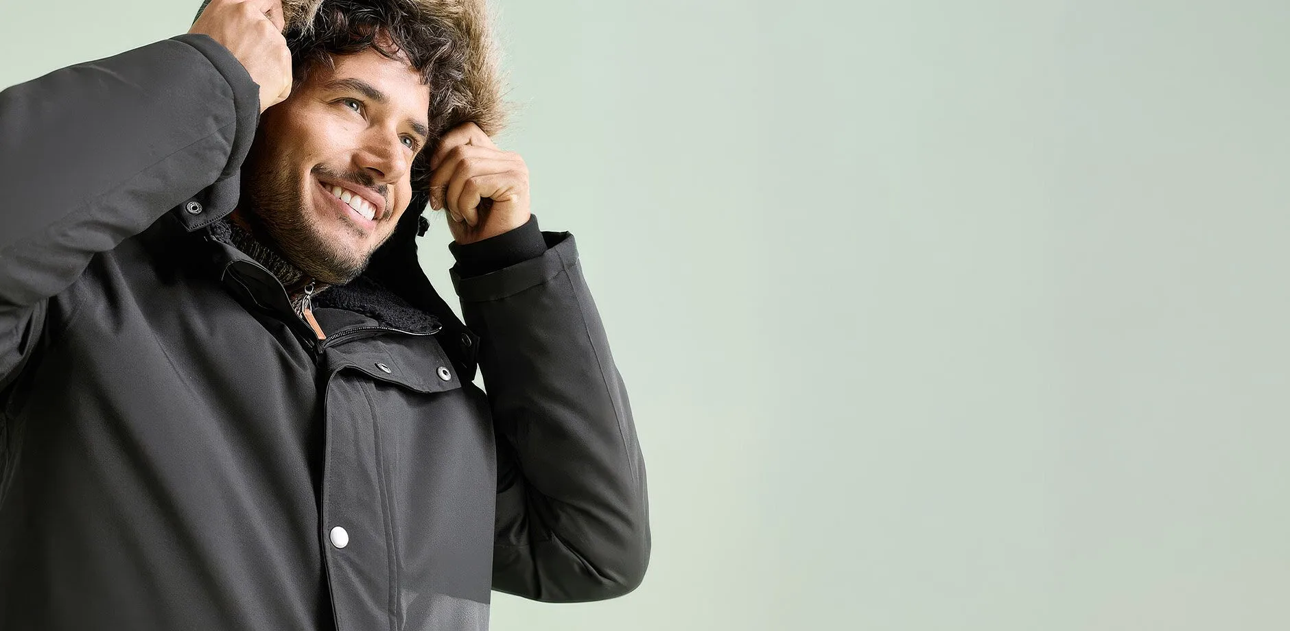 Er tr&auml;gt eine warme, dunkle Winterjacke mit kuscheliger Kapuze und Fellbesatz.