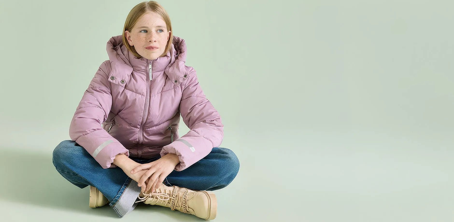 Rosa Steppjacke, blaue Jeans und beigefarbene Stiefel bilden ein warmes Outfit.