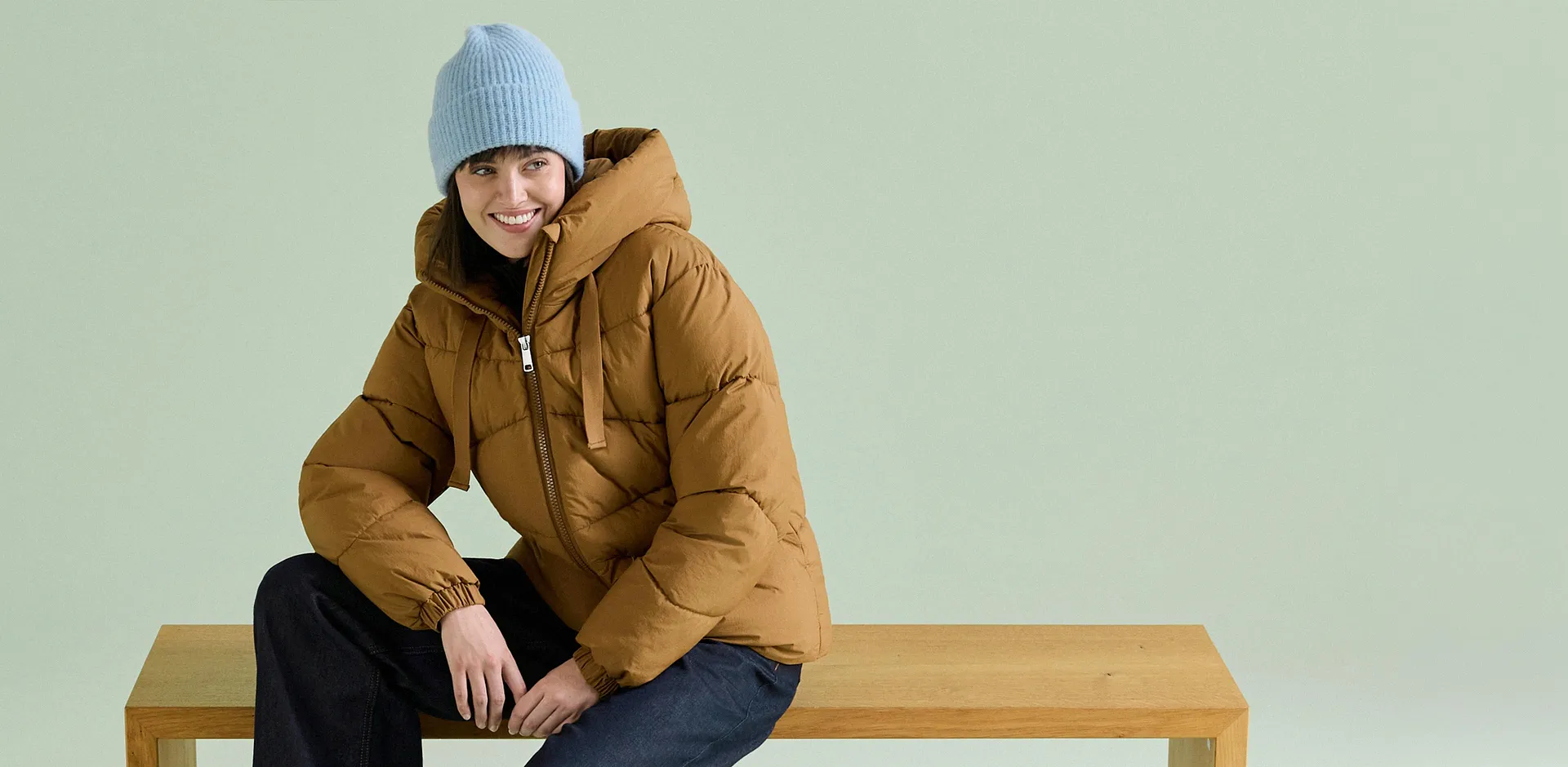 Die Person tr&auml;gt eine hellblaue M&uuml;tze, eine braune Steppjacke und dunkle Jeans.