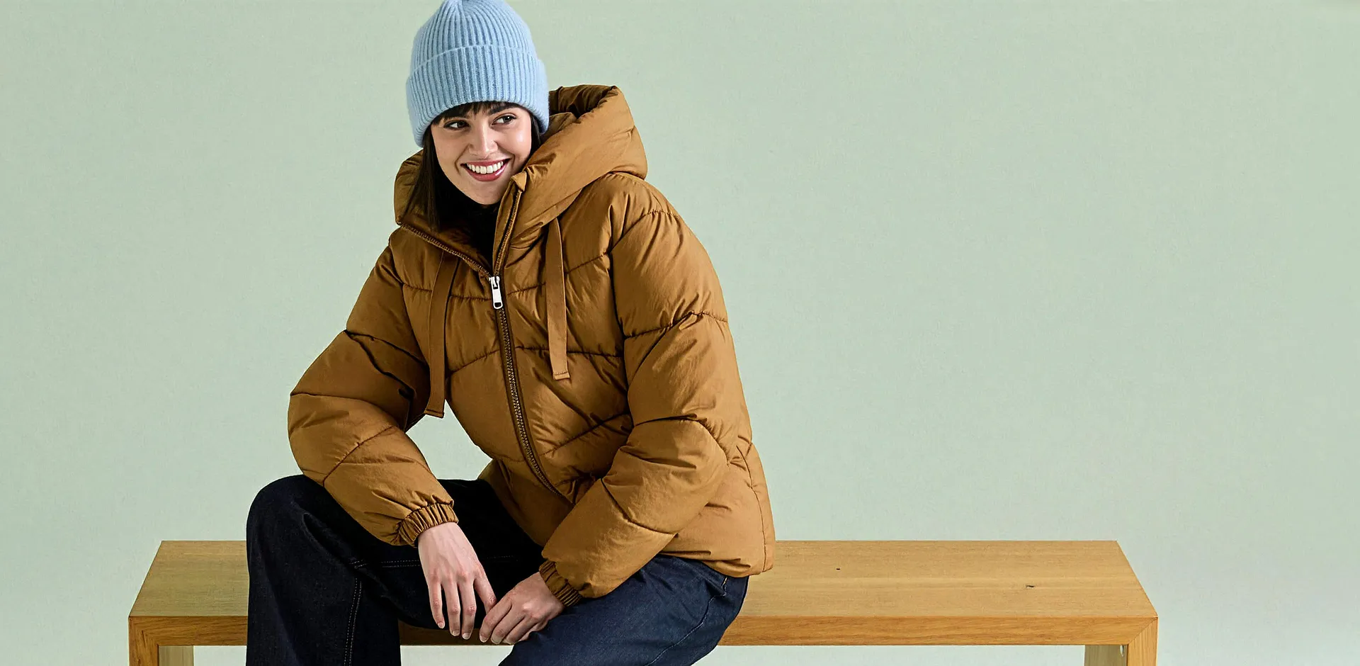 Die Person tr&auml;gt eine hellblaue M&uuml;tze, eine braune Steppjacke und dunkle Jeans.