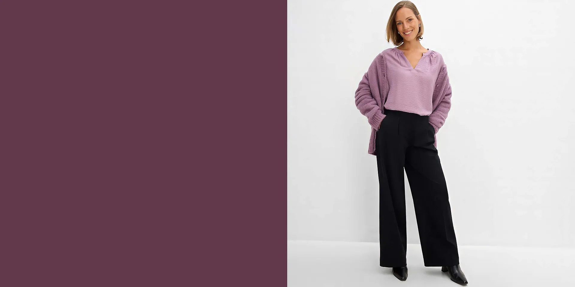 Sie tr&auml;gt eine lila Bluse, dazu einen Strickcardigan und eine schwarze weite Hose.