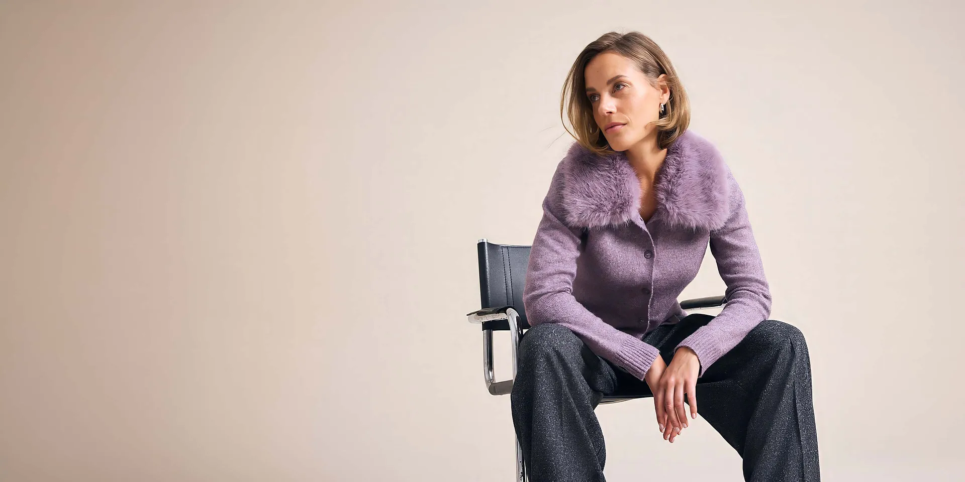 Fliederfarbene Strickjacke mit Fellkragen und glitzernde Hose, ein stilvoller Look.