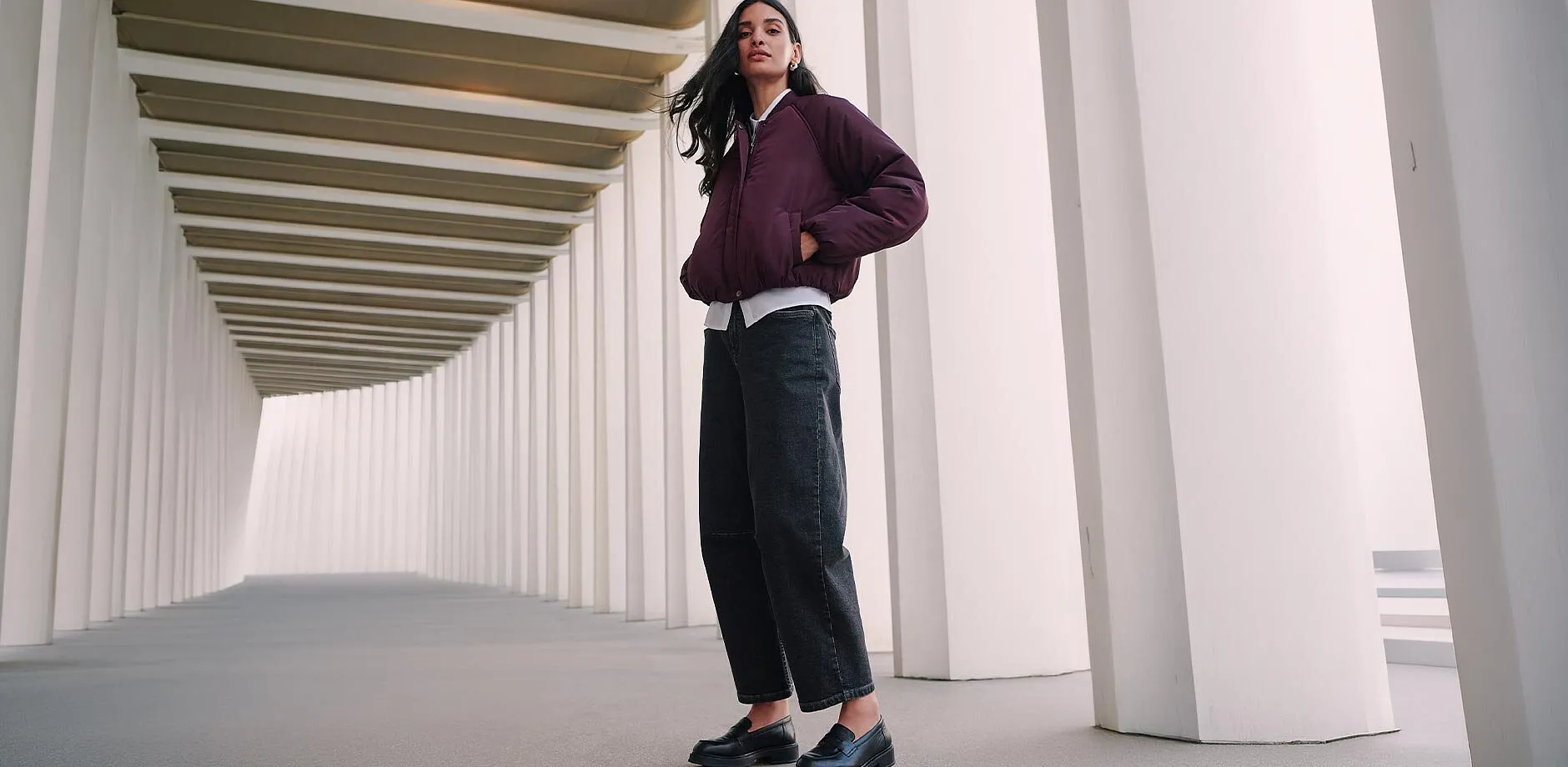 Dunkle Kappe, gesteppte bordeauxrote Jacke, roter Cardigan und dunkle Jeans.
