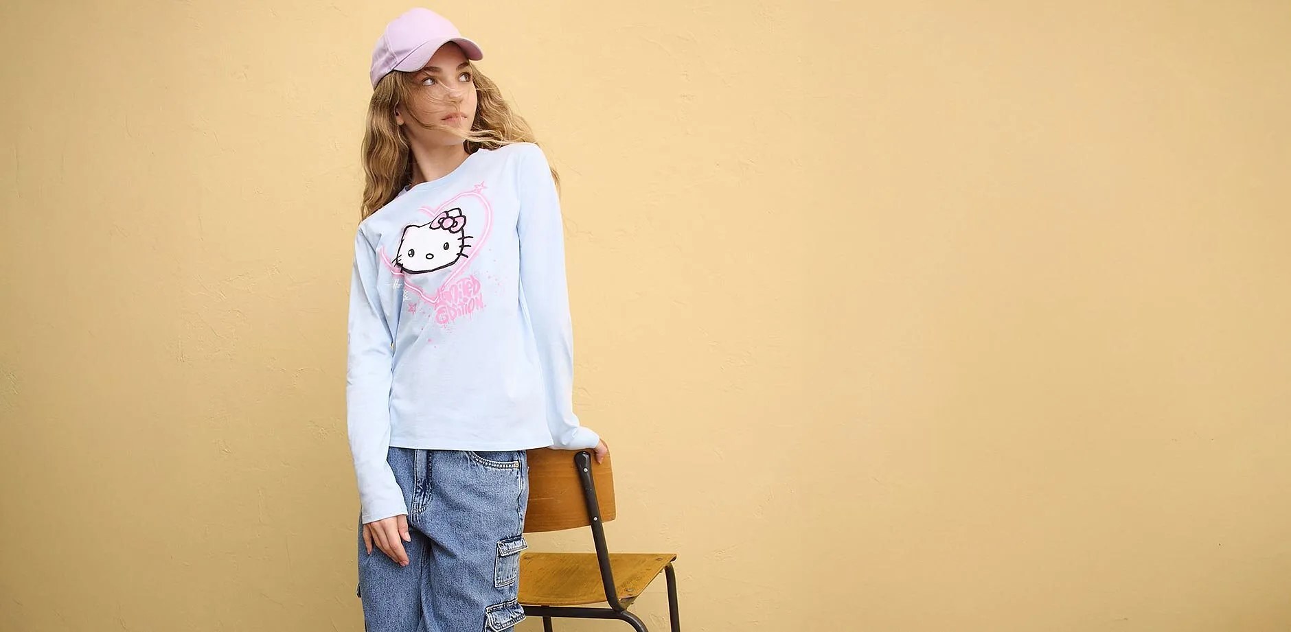 Blaues Langarmshirt mit Hello Kitty Aufdruck, blaue Jeans und rosa Cap.