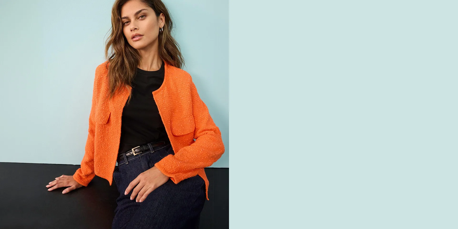 Gilet en maille orange vif port&eacute; sur un top noir, associ&eacute; &agrave; un jean et une ceinture chic.