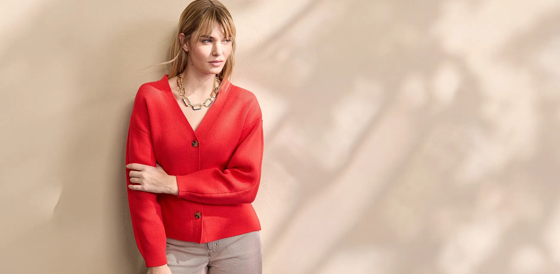 Eine leuchtend rote Strickjacke mit V-Ausschnitt und Kn&ouml;pfen, kombiniert mit einer auff&auml;lligen Goldkette.