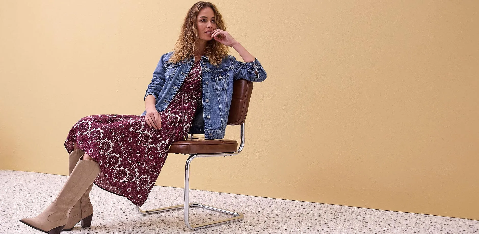 Veste en jean par dessus une robe longue &agrave; fleurs, associ&eacute;e &agrave; des bottes beige.