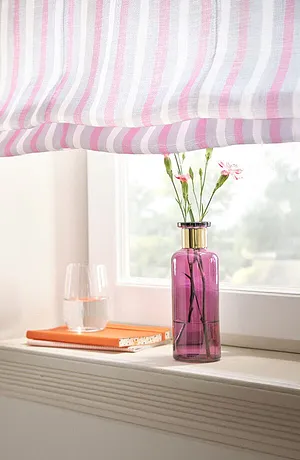 Fenêtre ornée de rideaux à rayures dans des tons pastel. En dessous, un vase de couleur rose avec des fleurs.