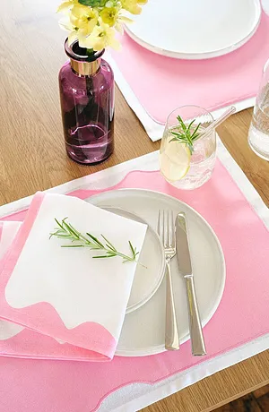 Table ornée d'une nappe rose à motif blanc. Des fleurs fraîches et des herbes aromatiques ajoutent une touche déco.