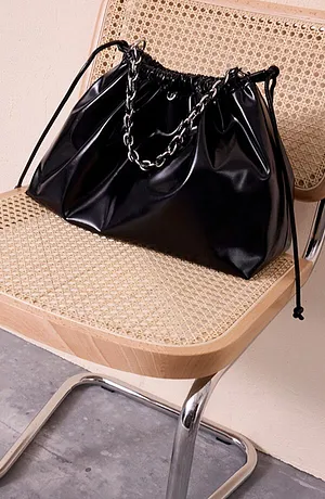Sac noir brillant avec une anse-chaîne sur une chaise en bois