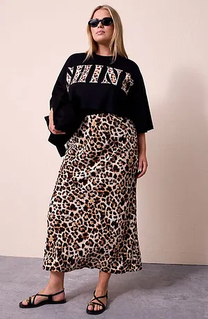 Femme portant un T-shirt crop noir avec SHINE en lettres léopard, jupe assortie à motif léopard, lunettes de soleil noires et sac noir brillant
