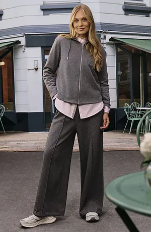 Pull gris à capuche par dessus un chemisier rose tendre, associé à un pantalon large gris et des sneakers blanches.