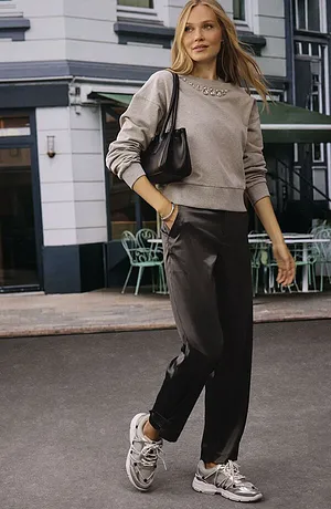 Style urbain décontracté : pull beige, pantalon foncé et sneakers blanches. Sac à main noir pour l'accessoire mode.