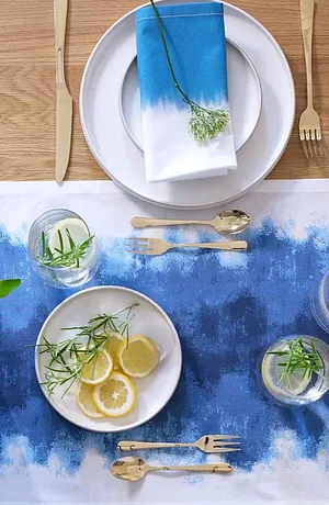 Un chemin de table bleu avec dégradé de couleur décore la table, complété de vaisselle blanche et de couverts raffinés.