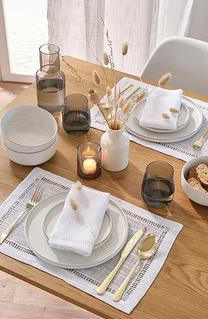 Une nappe de table élégante à motif dentelle, des serviettes blanches en tissu et des couverts de couleur dorée apportent une touche chic.