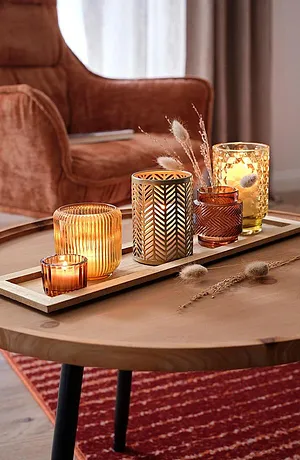 Gemütliche Herbststimmung mit warmen Kerzen und goldenen Dekorationen auf einem rustikalen Holztisch.