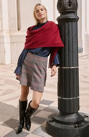 Écharpe rouge, blouse bleu foncé, jupe à carreaux et bottes noires.