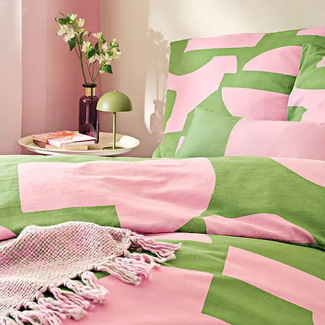 Linge de lit rafraîchissant en rose et vert, imprimé avec des formes géométriques. Une couverture tissée complète l'ensemble.
