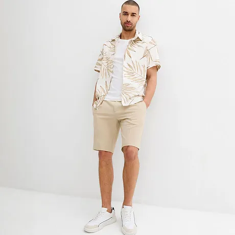 Sommerliches Outfit mit beigefarbener Shorts, weißem Hemd mit tropischem Muster.