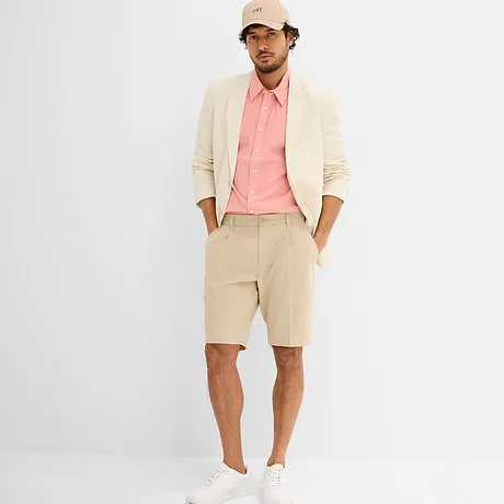 Elegantes  Sakko in Creme mit rosafarbenem Hemd, weißen Sneakern und beiger Kappe.
