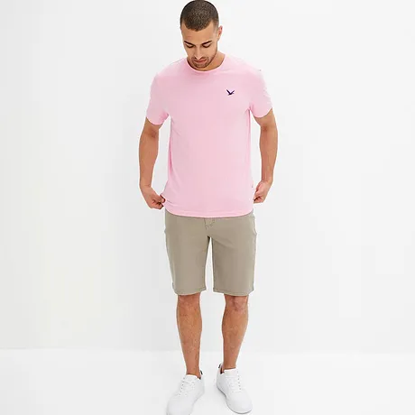 Ein rosa T-Shirt mit kleinem Logo und beige Shorts bilden ein sommerliches Outfit.