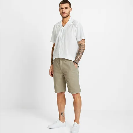 Weißes Kurzarmhemd mit Muster, beige Shorts und weiße Sneaker.