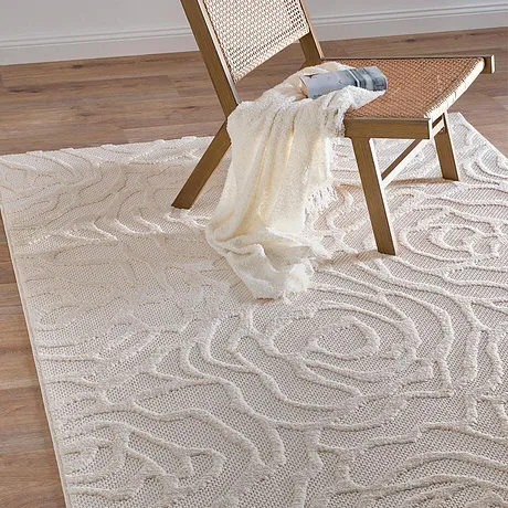 Un plaid léger couleur crème sur une chaise en rotin, sur un élégant tapis aux motifs ondulés.
