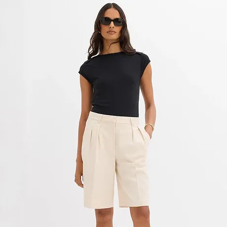 Association élégante d’un T-shirt noir et d’un bermuda crème.