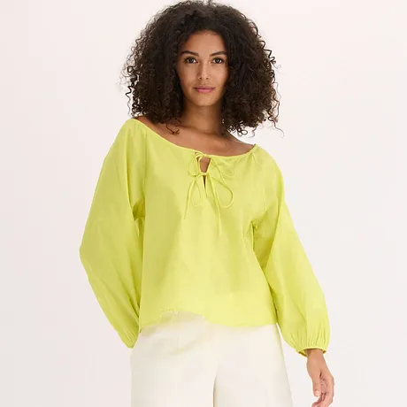 Blouse jaune citron légère à manches larges et détail à nouer sur l’encolure, avec un pantalon blanc.