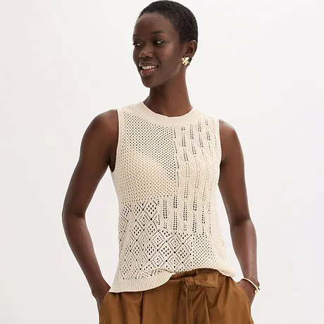 Un top crème en maille légère et sans manches sur un pantalon large et élégant de couleur rouille.
