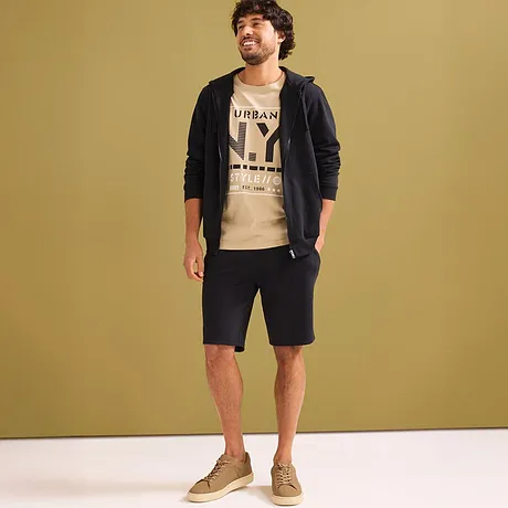 Lässiger Look mit beigem T-Shirt, schwarzer Kapuzenjacke & dunklen Sweat-Shorts.