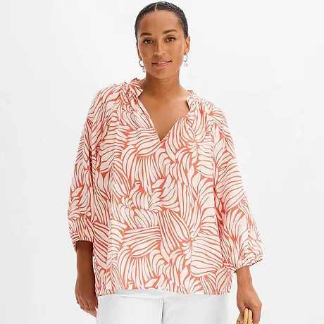Une blouse légère à motif palmier orange et un pantalon blanc.
