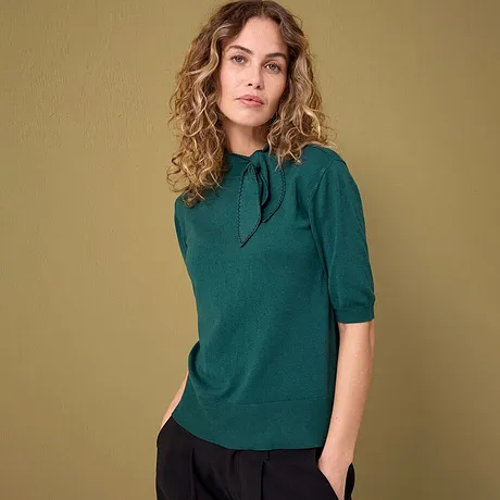 Un pull émeraude élégant à manches courtes associé à un pantalon foncé.