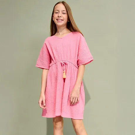 Robe rose estivale à manches courtes, cordon de serrage à la taille et pompons. Complétée par une paire de sandales dorées.