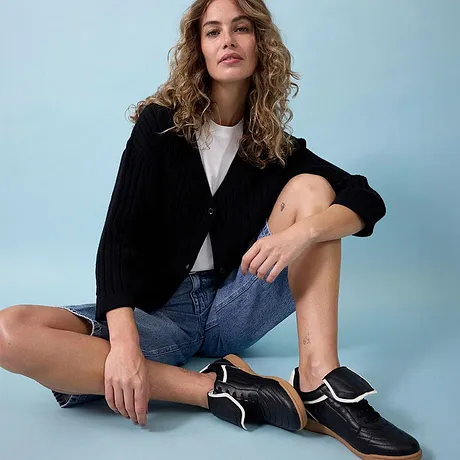 Gilet noir, T-shirt blanc, short en jean et une paire de tennis noires stylées.