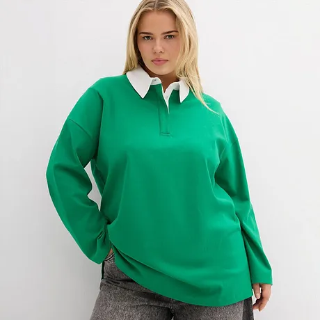 Smaragdgrünes Poloshirts mit weißem Kragen, kombiniert mit grauer Hose.