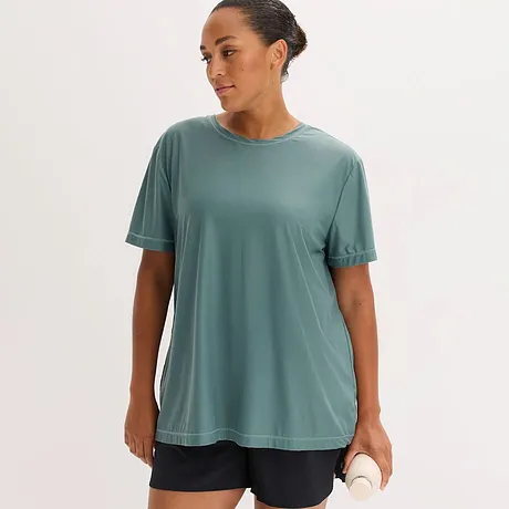 Ein lockeres, salbeigrünes Funktionsshirt mit Rundhalsausschnitt und kurzen Ärmeln, kombiniert mit dunklen Shorts.
