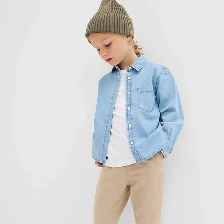 Chemise en jean bleu clair sur un T-shirt blanc, pantalon beige et bonnet en maille vert : un look enfant mode.