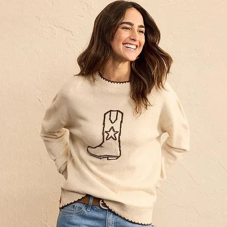 Pull couleur crème à motif botte, associé à un jean bleu.