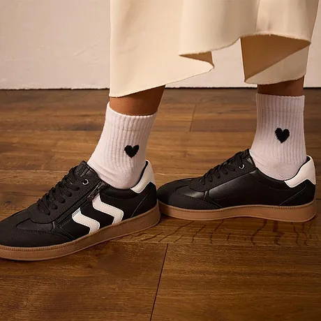 Chaussettes blanches à petits cœurs, tennis noires à rayures blanches. 