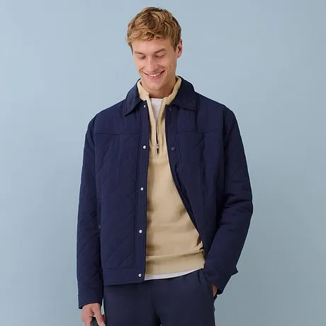 Dunkelblaue Steppjacke kombiniert mit einem beigefarbenem Pullover und blauer Hose.